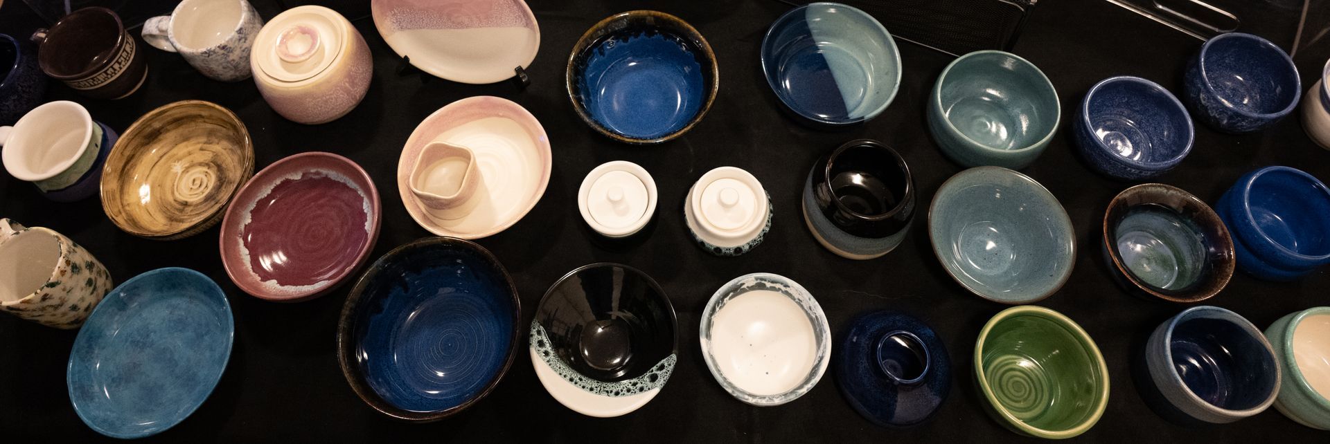 Various ceramic bowls in shades of blue, green, black, pink, and white displayed on a black surface.