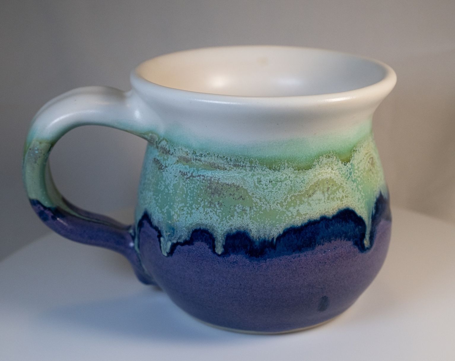 Ceramic mug with white, green, and blue glaze, sitting on a white surface.