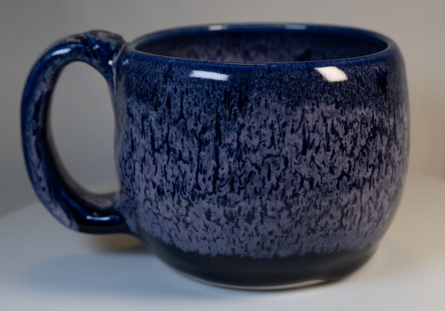 Blue and purple speckled ceramic mug with a large handle, sitting on a white surface.
