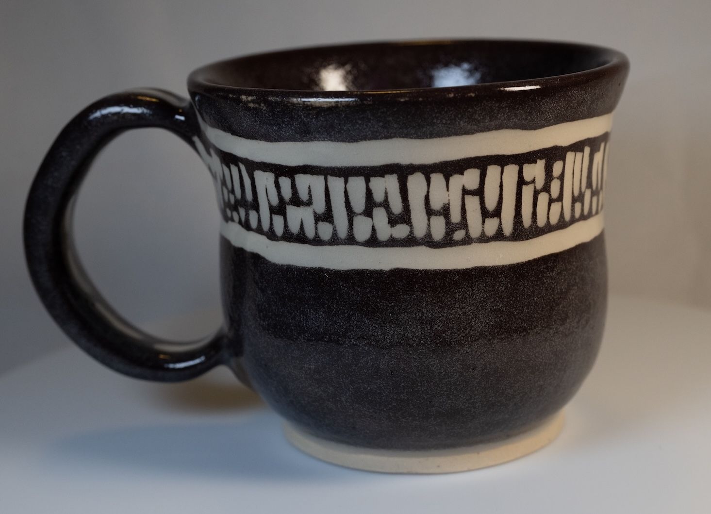 Dark ceramic mug with a white band of textured design, on a white surface.