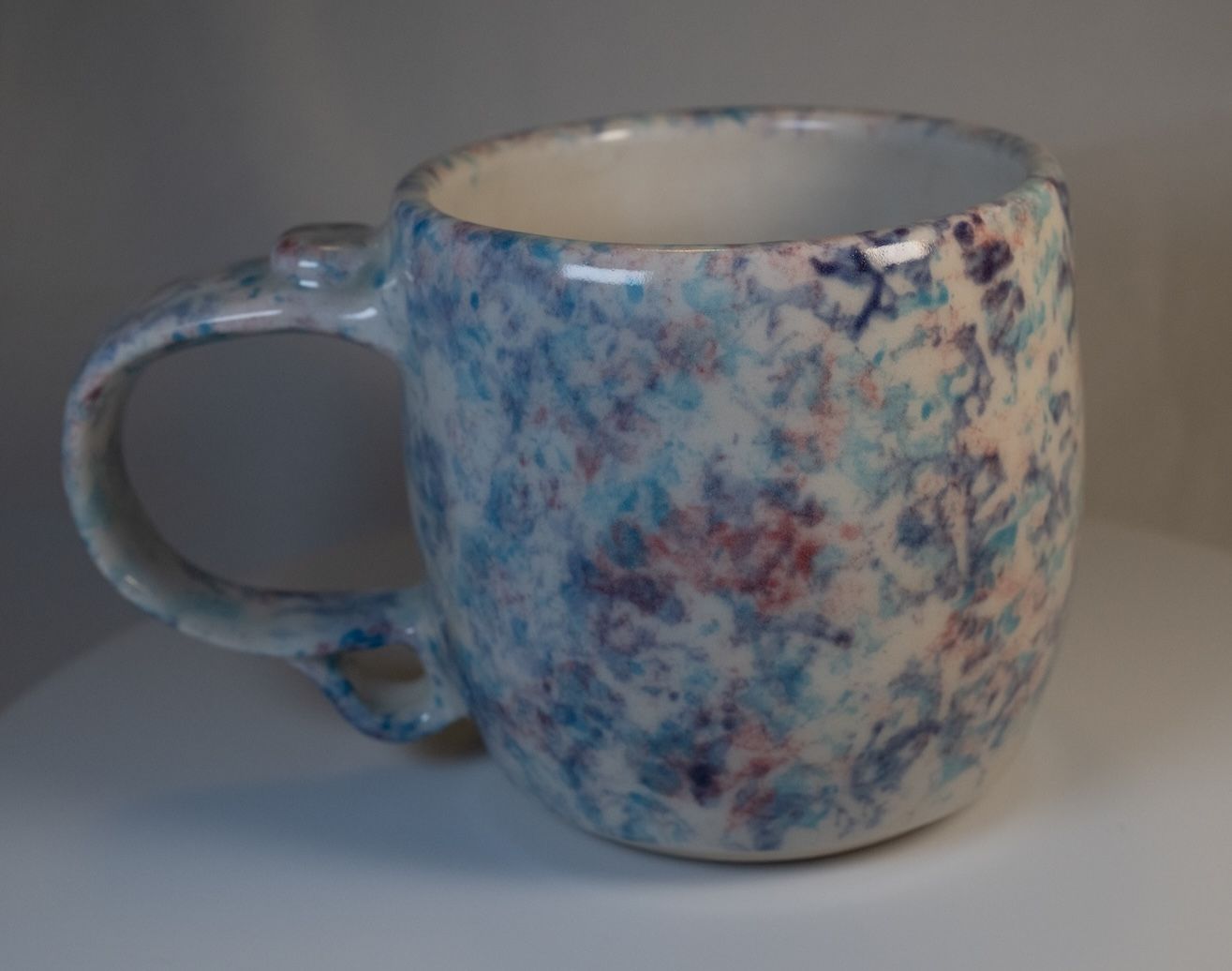Ceramic mug with speckled blue, purple, and white glaze; on a white surface.