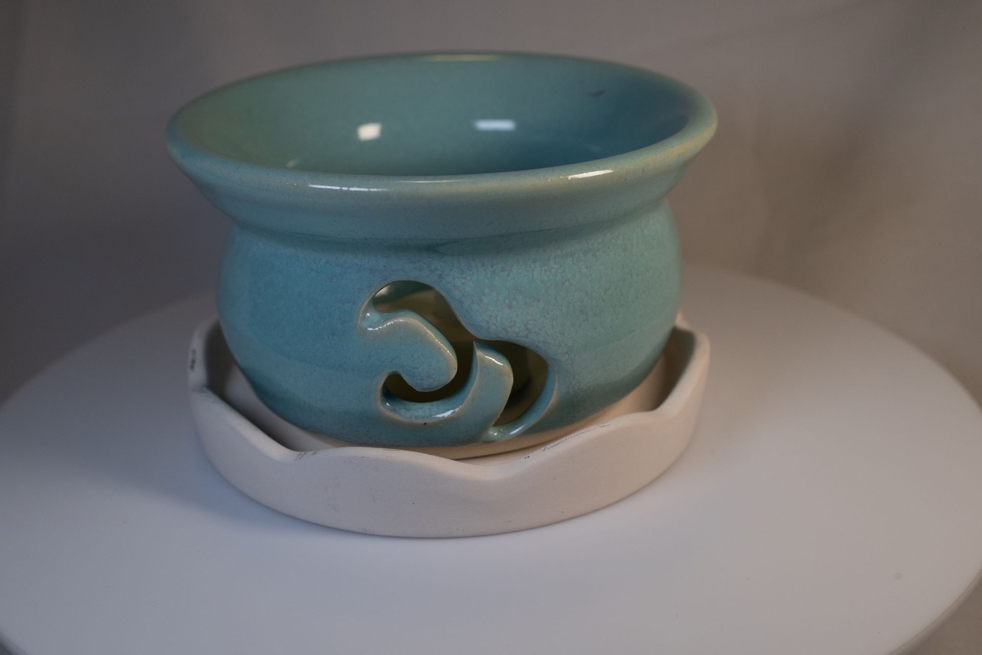 Teal ceramic oil warmer with cut-out design, sitting on a white wavy-edged dish.