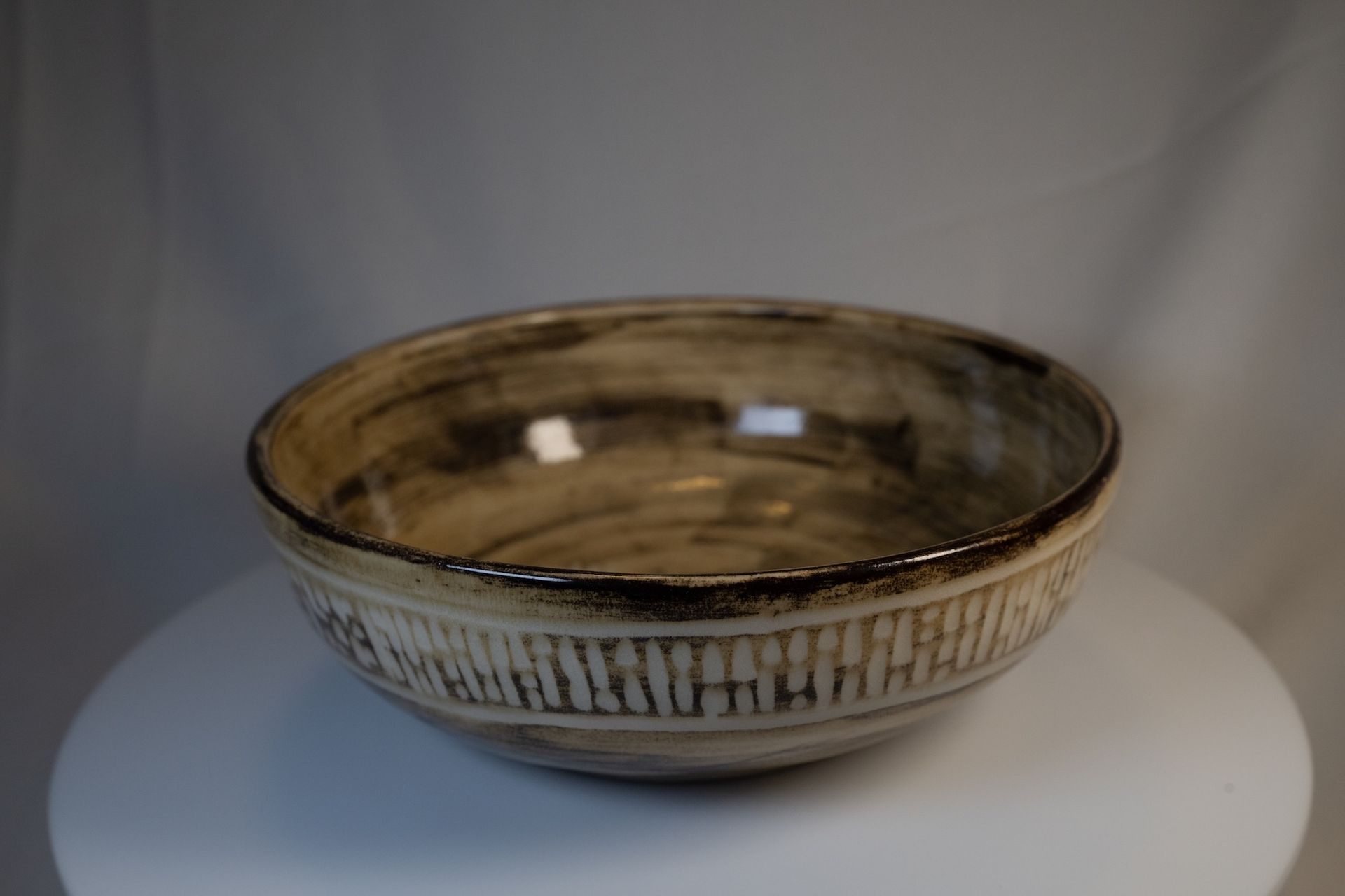 Ceramic bowl with textured vertical lines, brown and beige color scheme, set on a white surface.