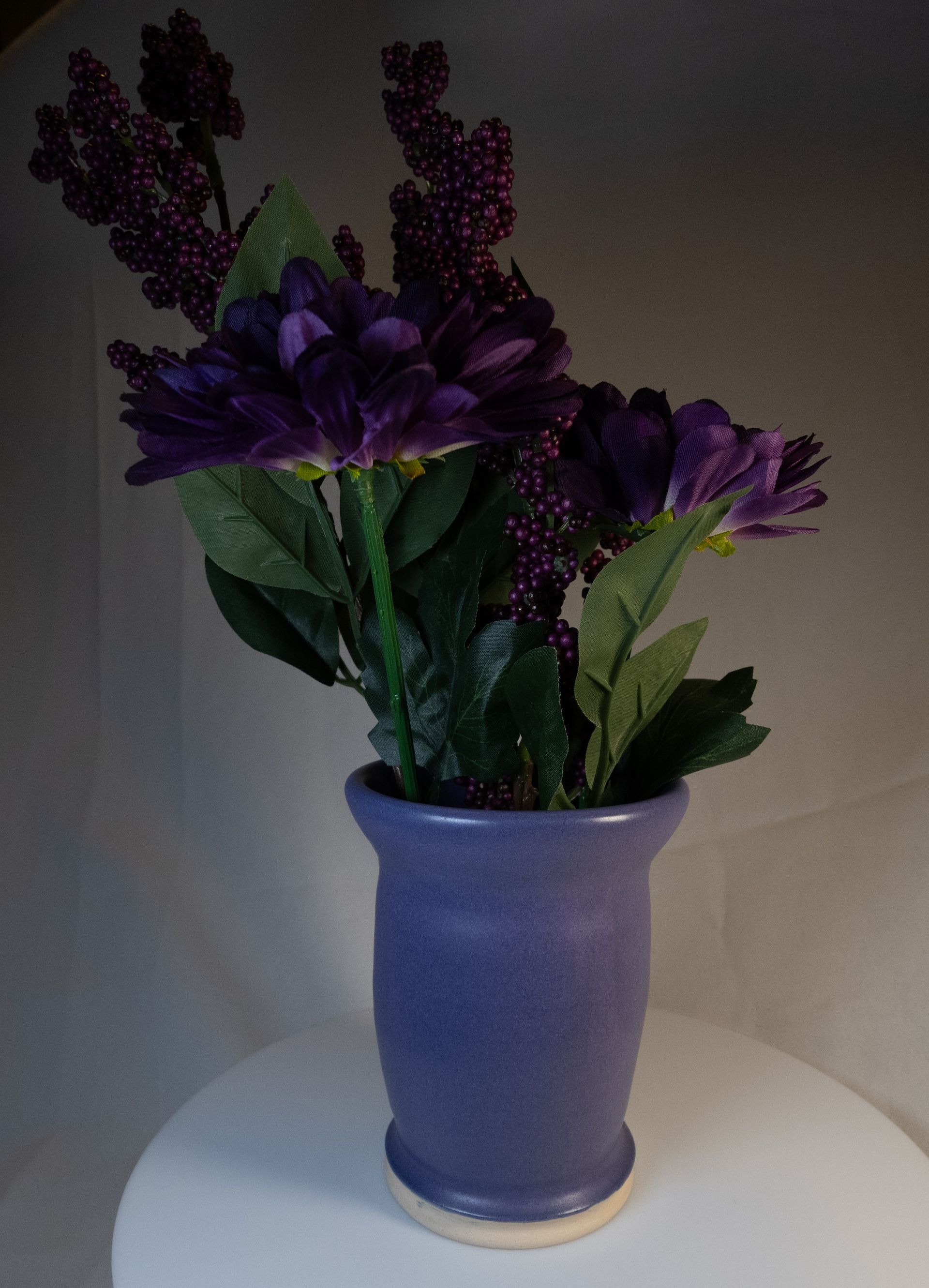 Purple flowers in a blue ceramic vase on a white surface.