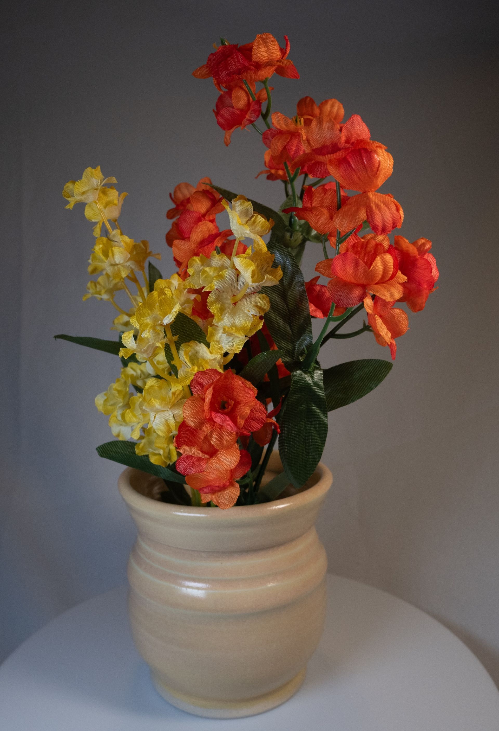 Tan vase with orange and yellow flowers.