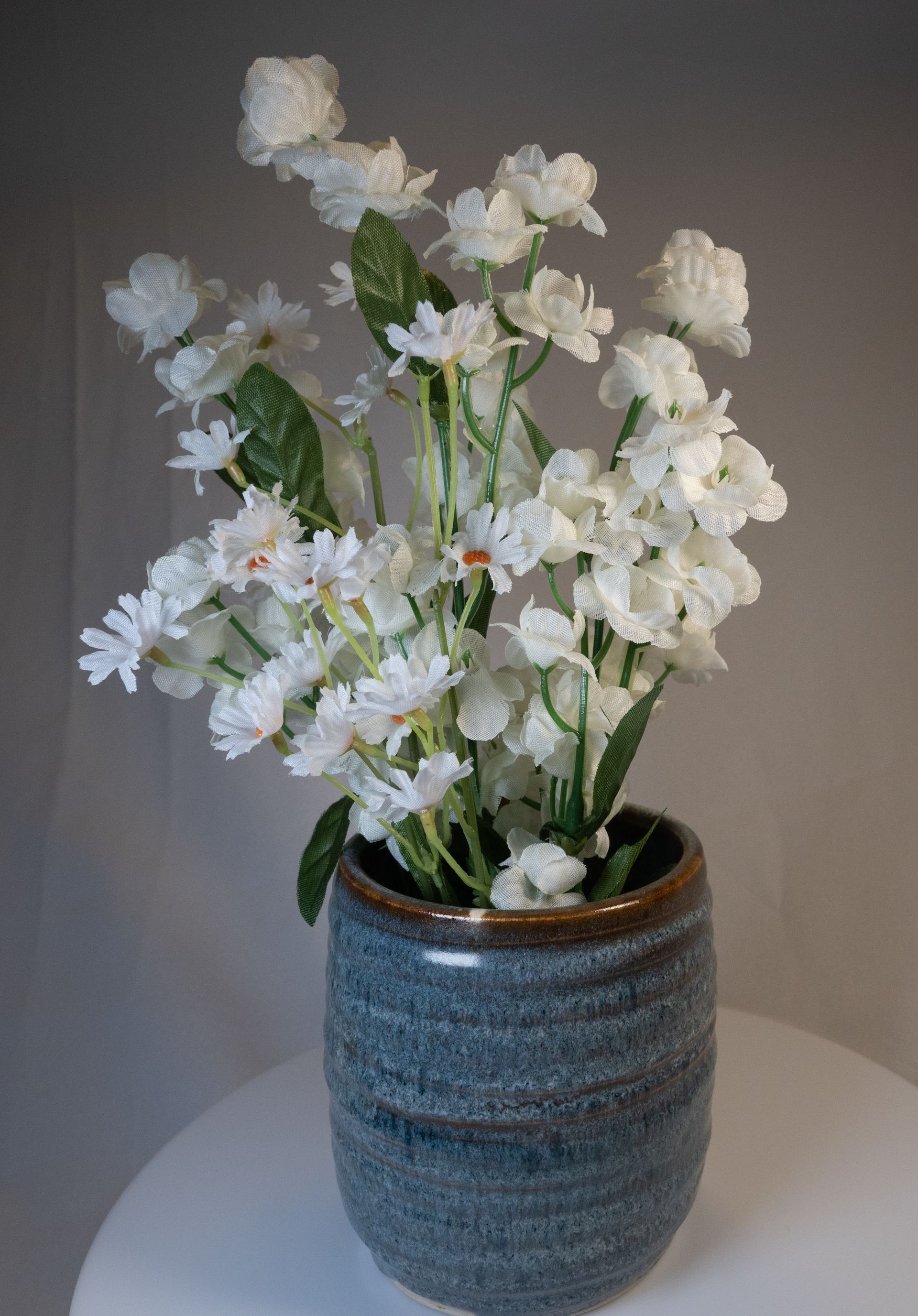 White flowers in a blue ceramic vase on a white surface.