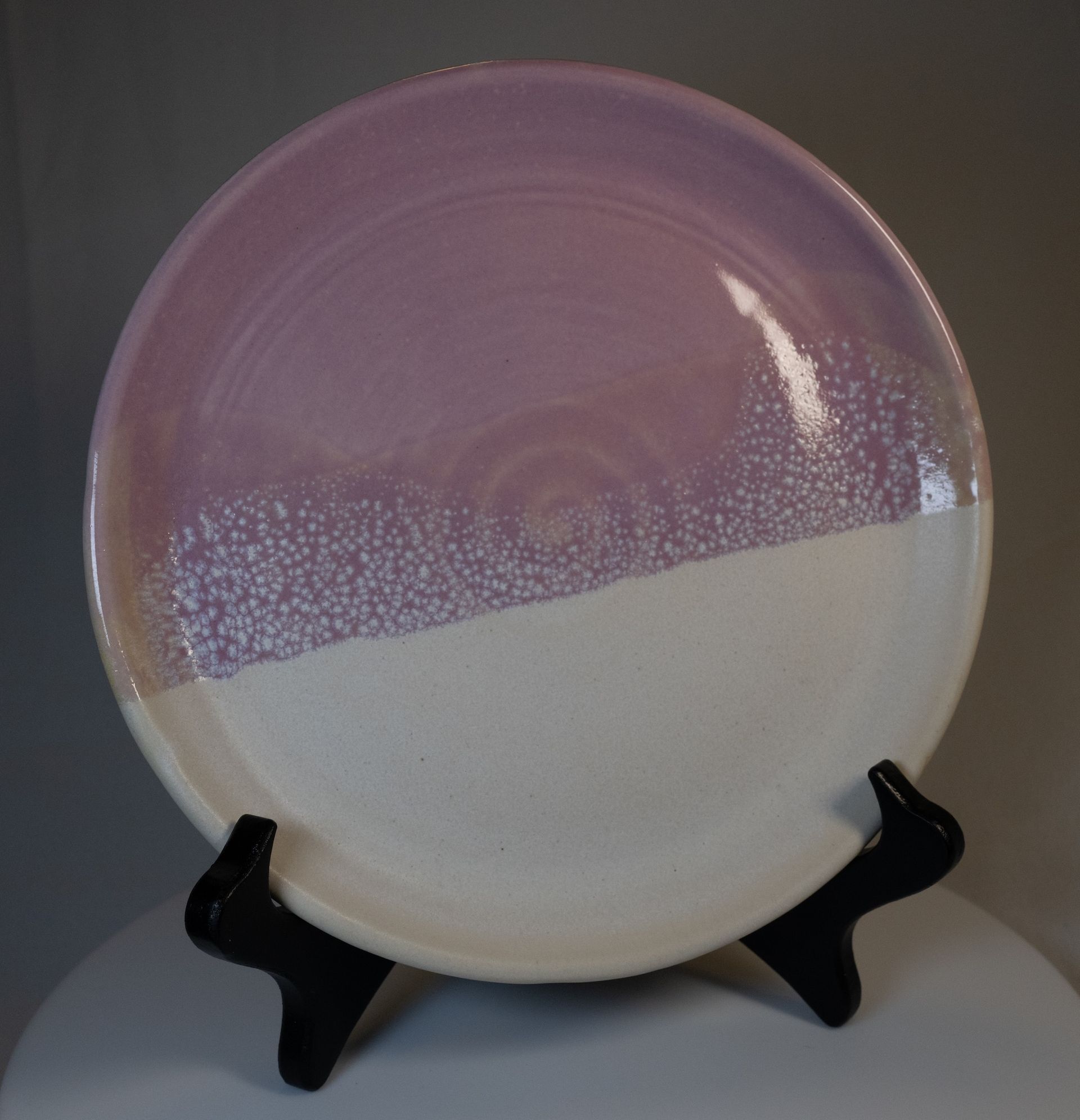 Purple and white ceramic plate on a black stand.