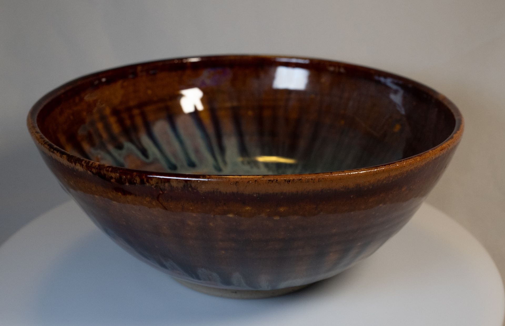 Brown glazed ceramic bowl, with iridescent blue and green interior, resting on white surface.