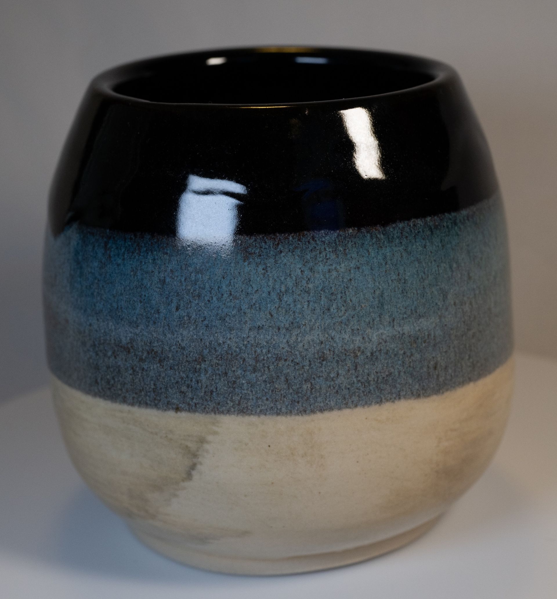 Ceramic cup with three horizontal color bands: black, blue, and beige.