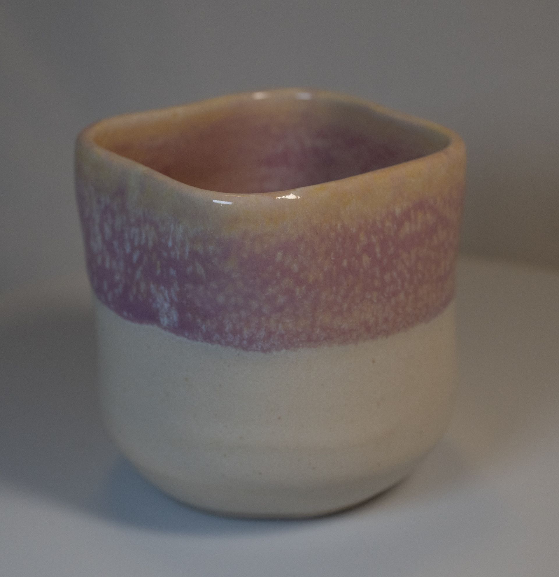 Small ceramic cup, white bottom, lavender band, yellow rim.