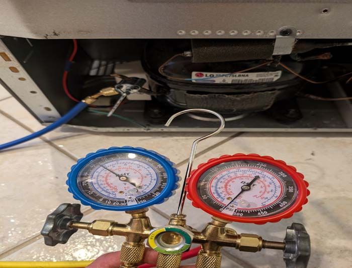 Refrigeration gauges connected to a fridge compressor for pressure readings, a blue and red gauge.