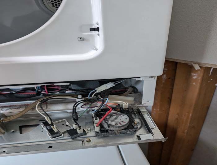 Interior of a dryer showing exposed wires, control panel, and metal frame. White appliance in a home setting.