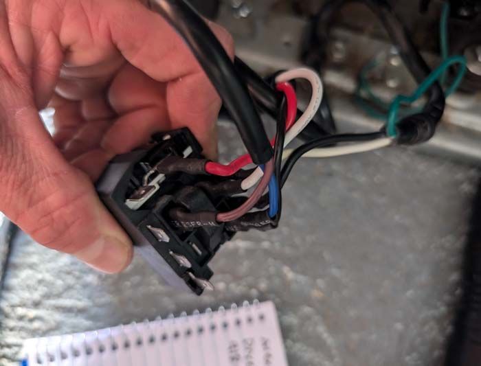 Hand holding an electrical switch with multiple wires attached. Colors: black, red, white, blue, green.