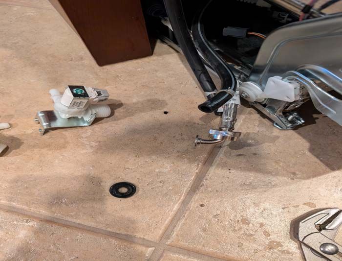 Dishwasher parts disassembled on the floor, including a water valve and a wrench, possibly for repair.