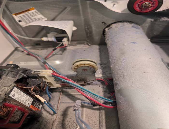 Inside of a dryer, with wiring, lint buildup, and a vent tube.