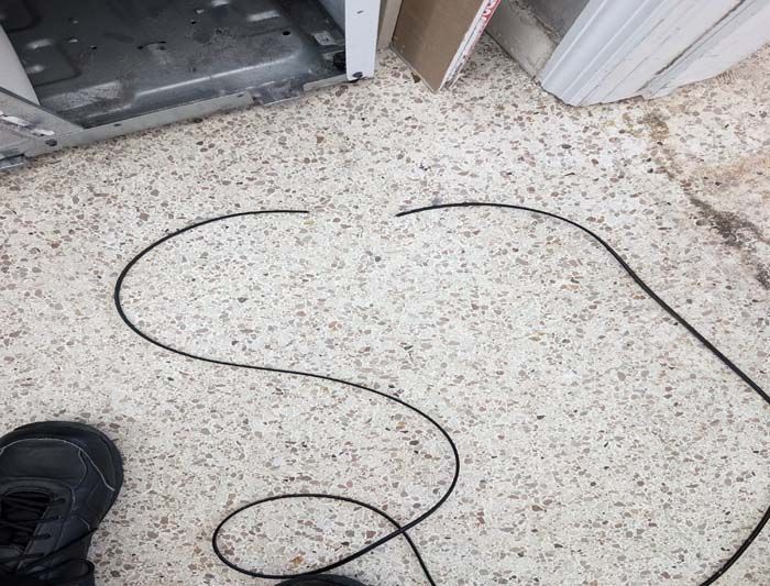 A black, cut cable on a speckled floor, near a door and a shoe.