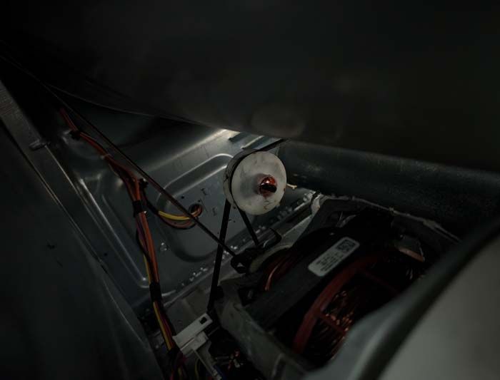 Inside a dryer: motor, pulley, belt, wiring. Dark setting, lit from above.