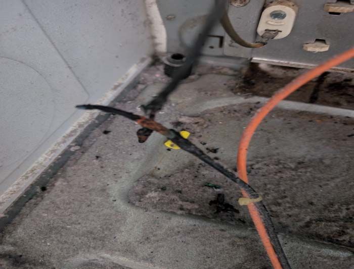 Damaged electrical wires inside a dirty appliance. Burnt and corroded black wire, yellow wire connectors.