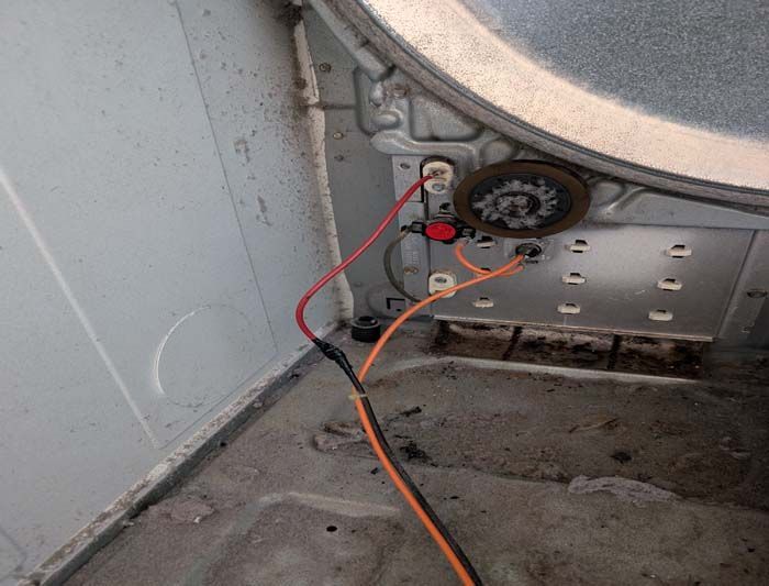 Inside of a dryer with exposed wires, a red button, and a circular thermostat.
