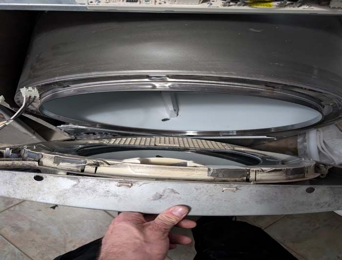 Washing machine drum disassembled; a person's hand holds a broken front panel.