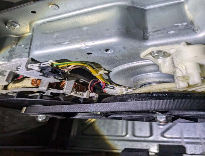 Internal view of a washing machine with wires, a belt, and mechanical components.