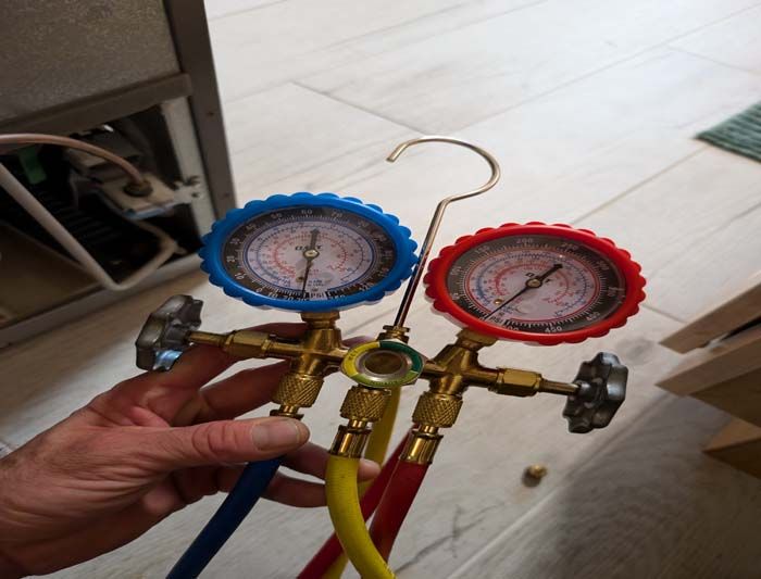 Hand holding a manifold gauge set with blue and red gauges, yellow, blue, and red hoses near appliance.