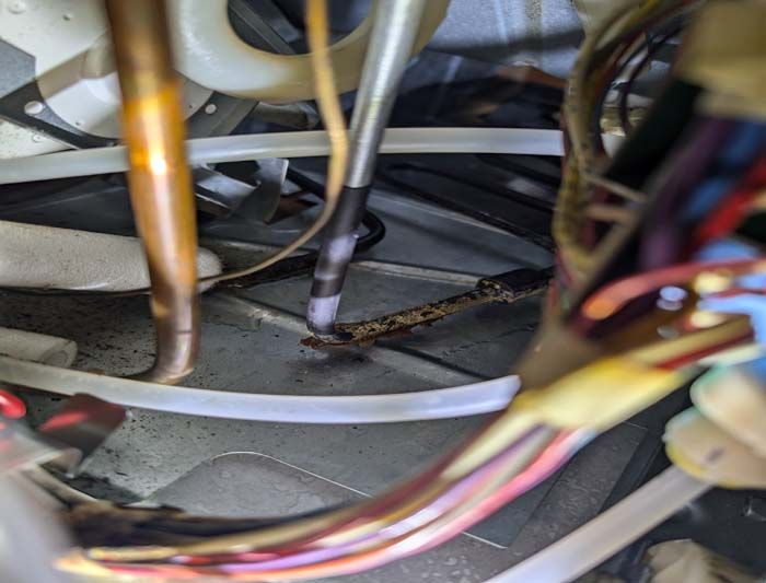Interior of a machine with copper pipes, wires, and a black tube. Close-up shot with focus on the wires and pipes.