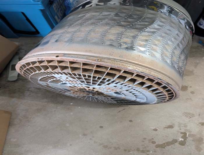 A large, circular, metal engine component with intricate honeycomb-like design, sitting on concrete.