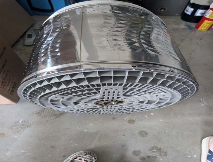 Shiny metal washing machine drum on concrete floor.