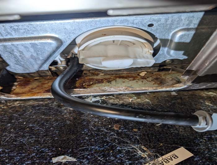 A close-up of a dishwasher pump filter, a black hose, and a rusted metal surface.