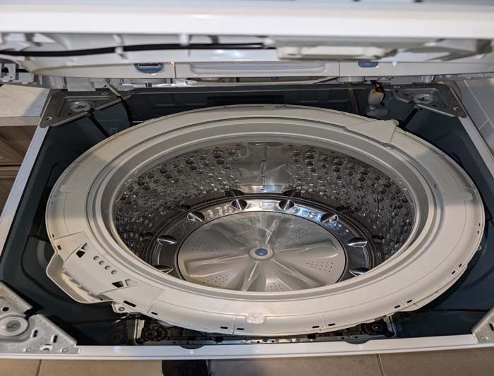 Interior of a top-load washing machine with the lid open, showing the tub, agitator, and surrounding frame.