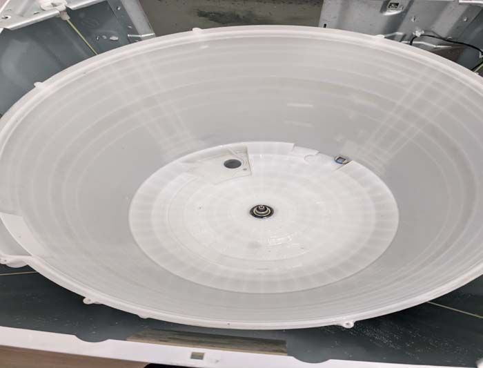 Interior view of a white washing machine tub, circular with a central drain and concentric ridges.