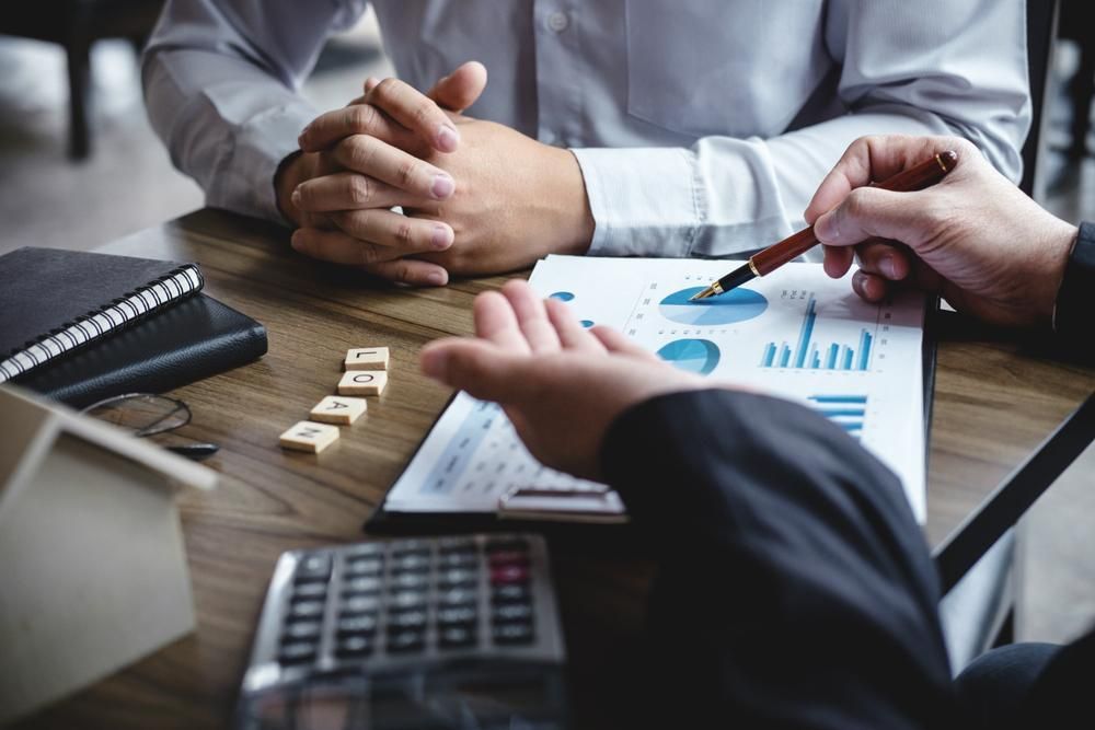 Two men are sitting at a table looking at a graph — Coast & Country Insurance Consultants Pty Ltd In Central Coast, NSW