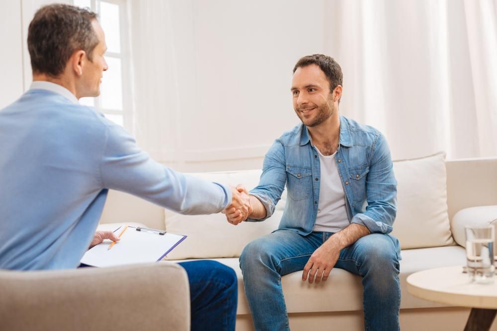 A Man Is Shaking Hands With Another Man While Sitting On A Couch — Coast & Country Insurance Consultants Pty Ltd In Central Coast, NSW