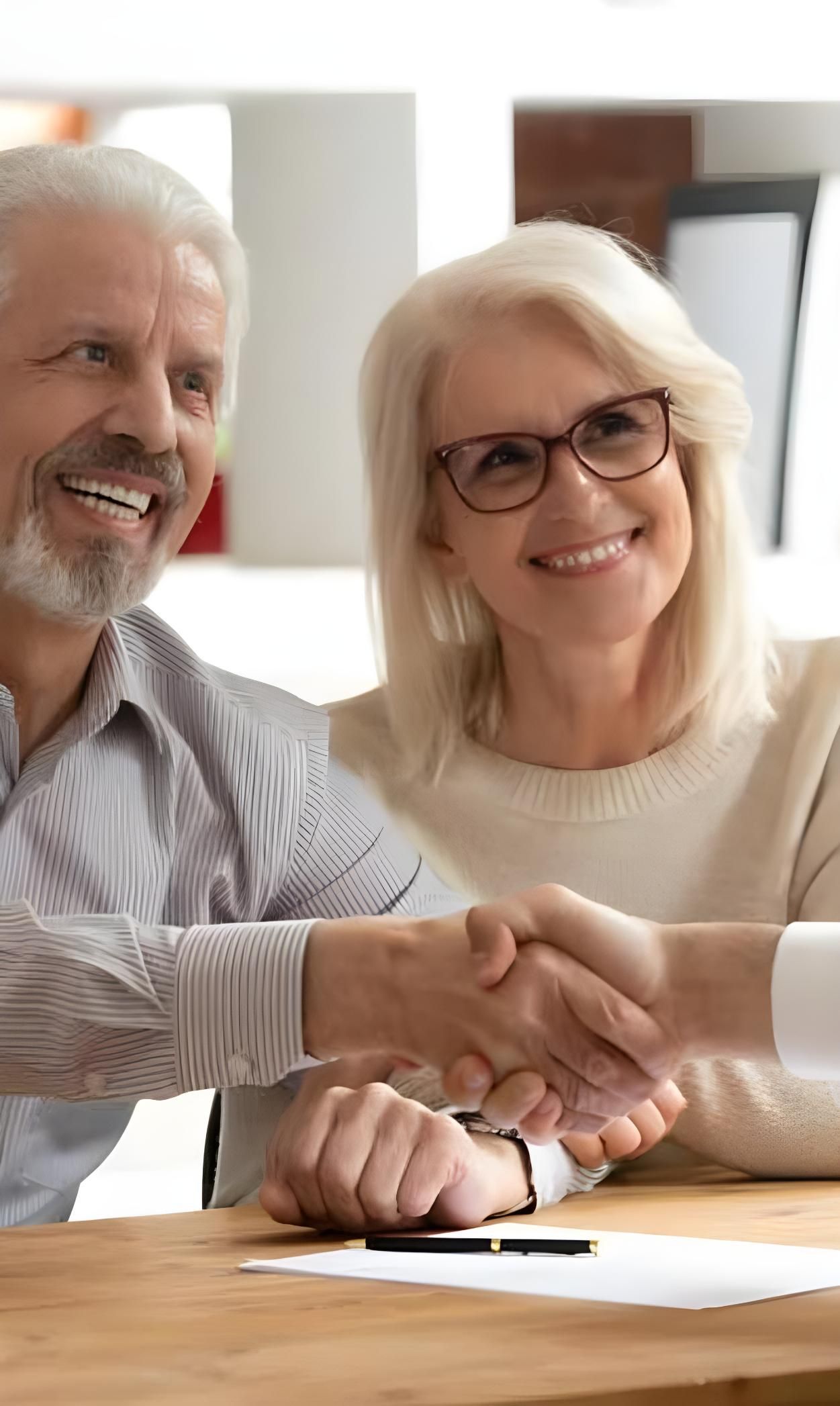 A man and a woman are shaking hands at a table — Coast & Country Insurance Consultants Pty Ltd In Central Coast, NSW