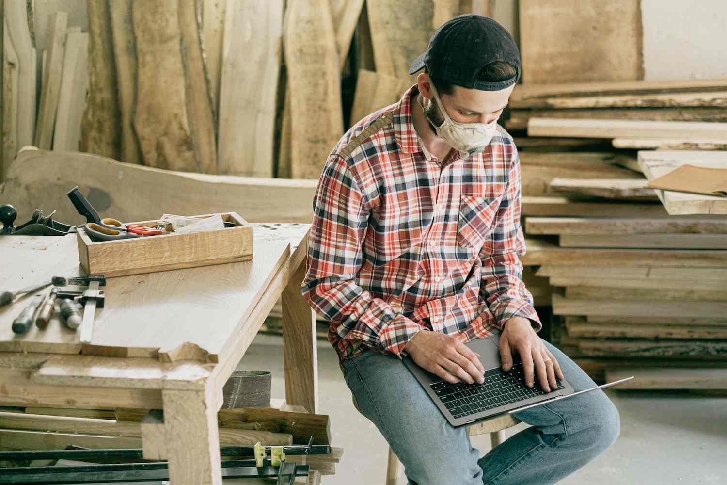 a Man Wearing a Mask is Sitting on a Bench Using a Laptop Computer — Coast & Country Insurance Consultants Pty Ltd In Central Coast, NSW
