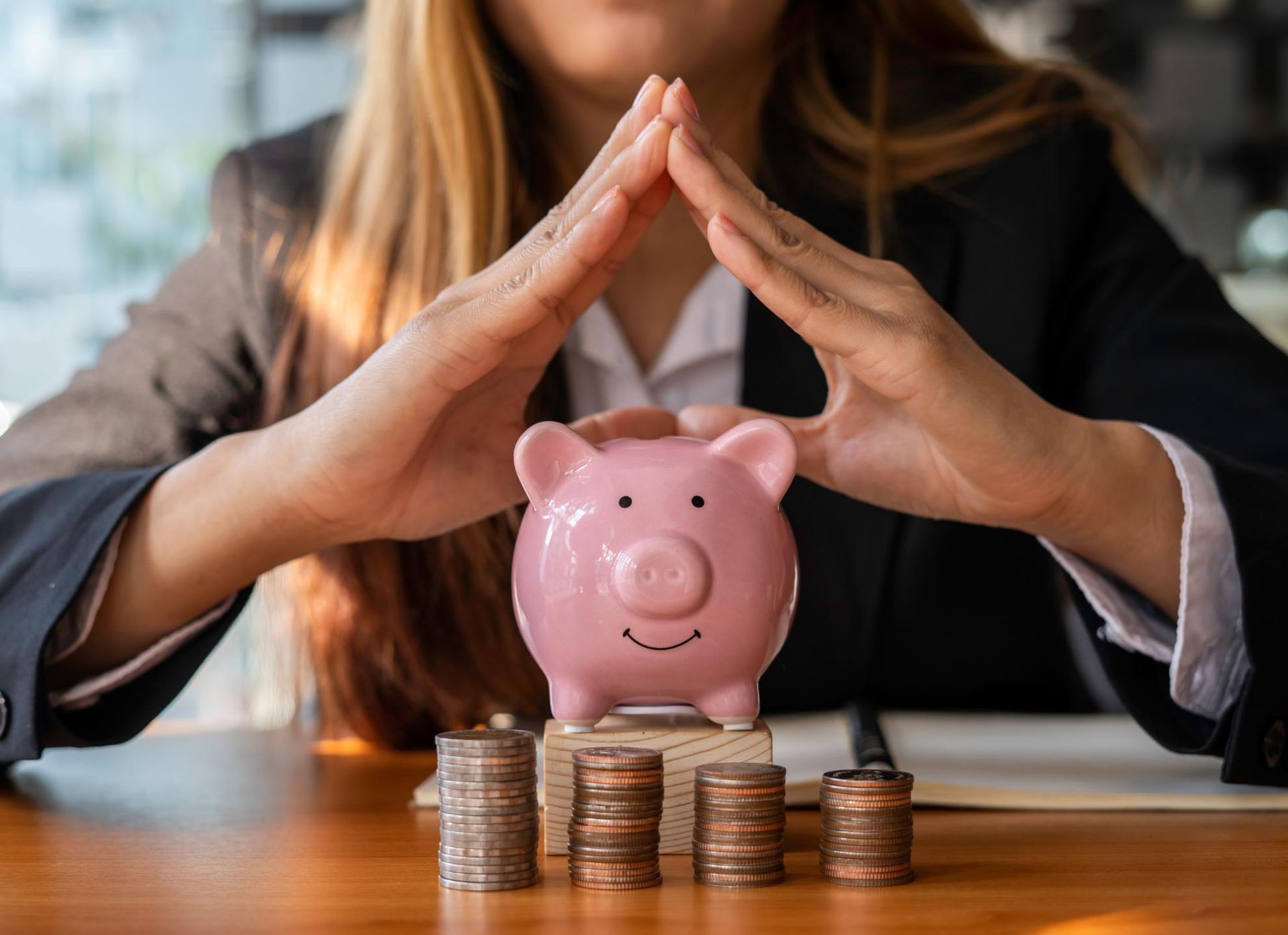 a Woman is Sitting at a Table With a Piggy Bank and Stacks of Coins — Coast & Country Insurance Consultants Pty Ltd In Central Coast, NSW