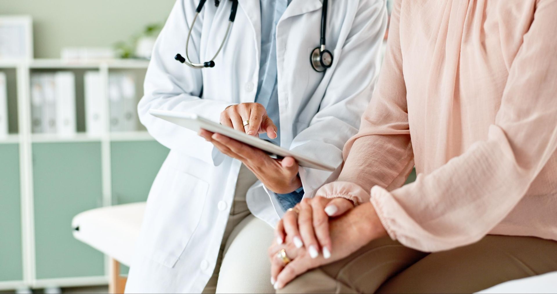 a Doctor is Holding the Hand of a Patient While Looking at a Tablet — Coast & Country Insurance Consultants Pty Ltd In Central Coast, NSW