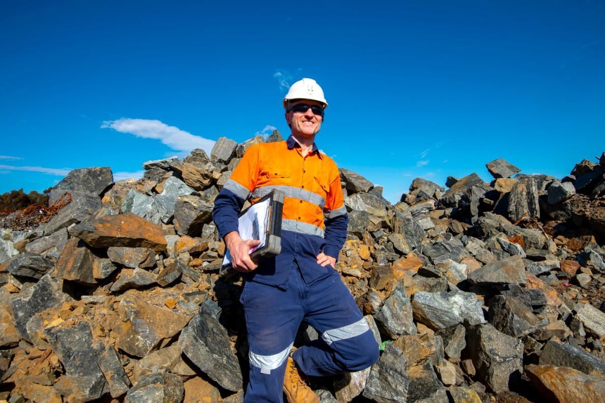 a Man in a Hard Hat is Sitting on a Pile of Rocks — Coast & Country Insurance Consultants Pty Ltd In Central Coast, NSW