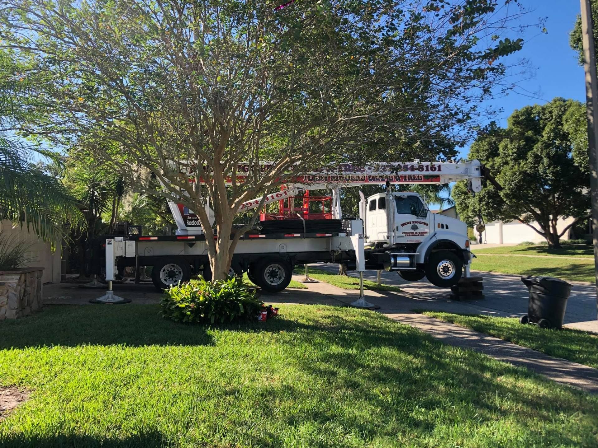 A white truck with a crane on the back is parked in front of a house.
