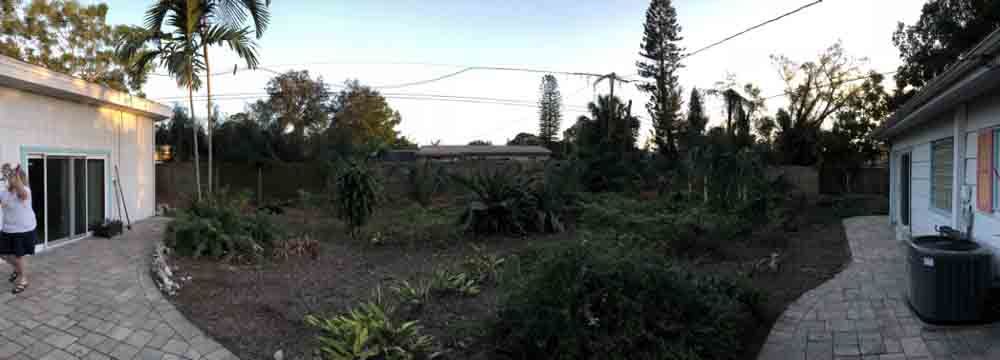 A panoramic view of a backyard with a brick walkway leading to a house.