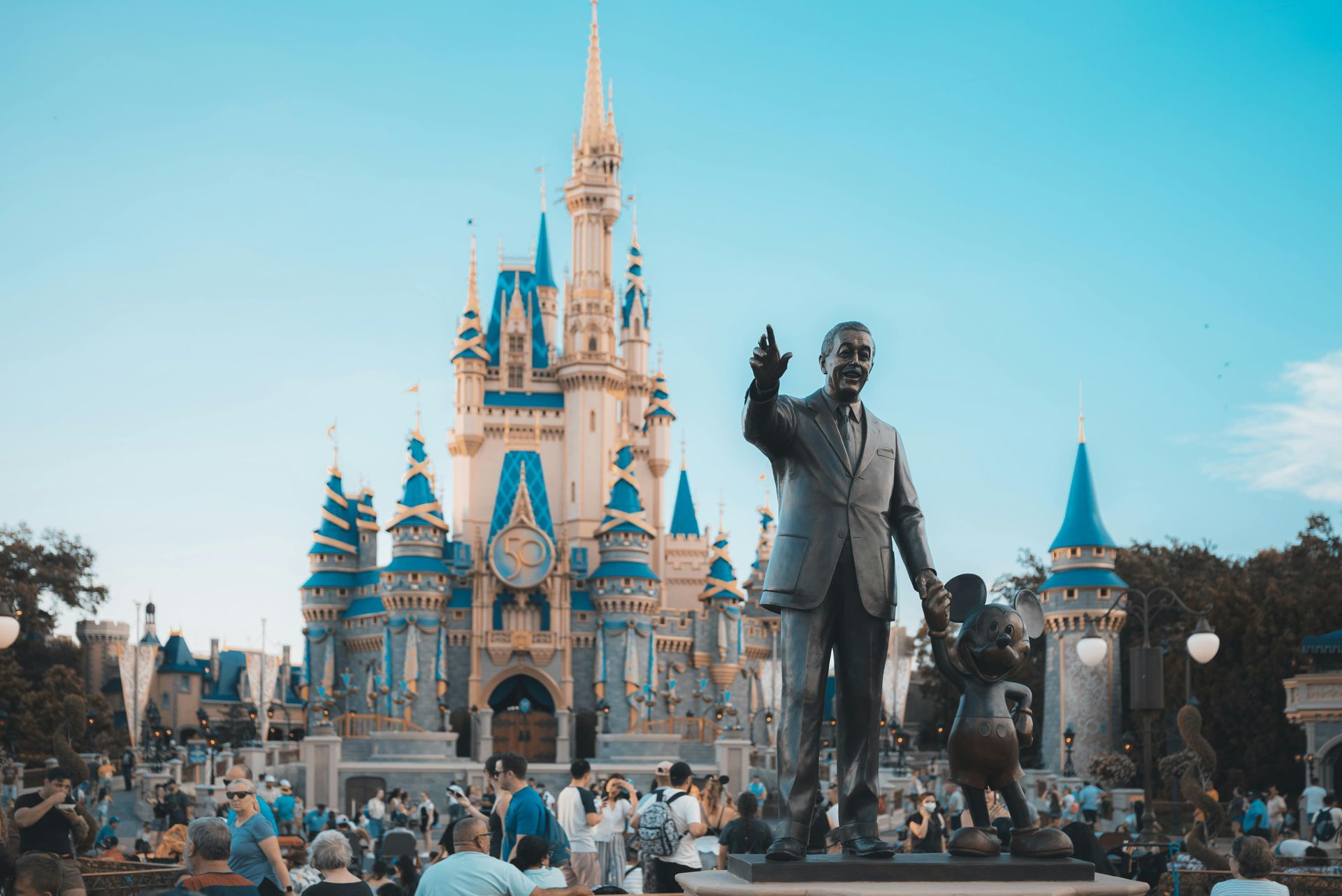 Crowd in front of Cinderella Castle and Walt Disney statue at Disneyland under a clear blue sky