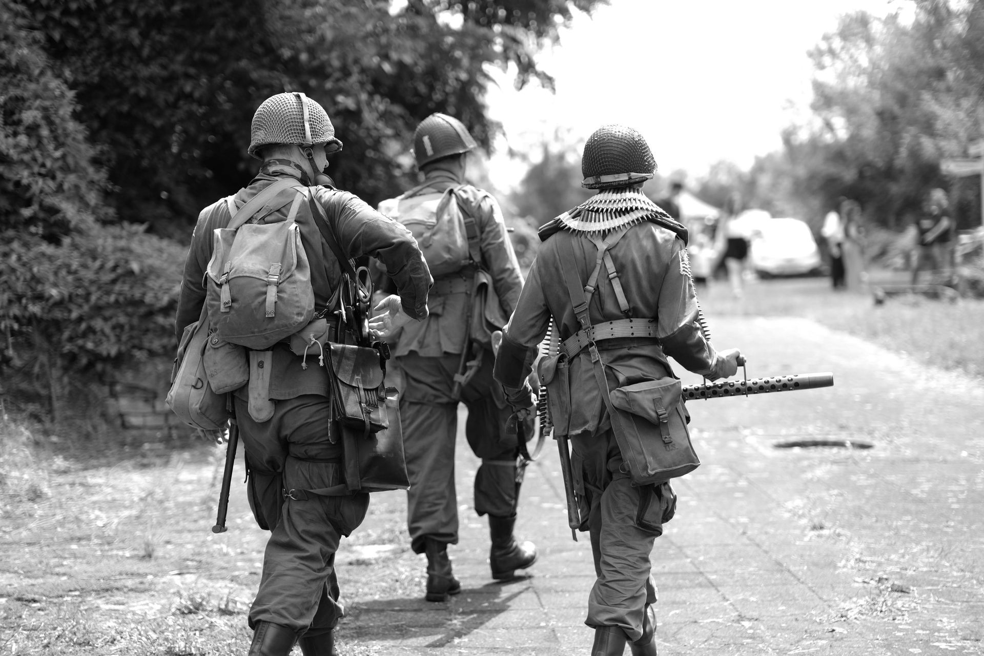 Three soldiers in camouflage walk down a wet road carrying gear and rifles.
