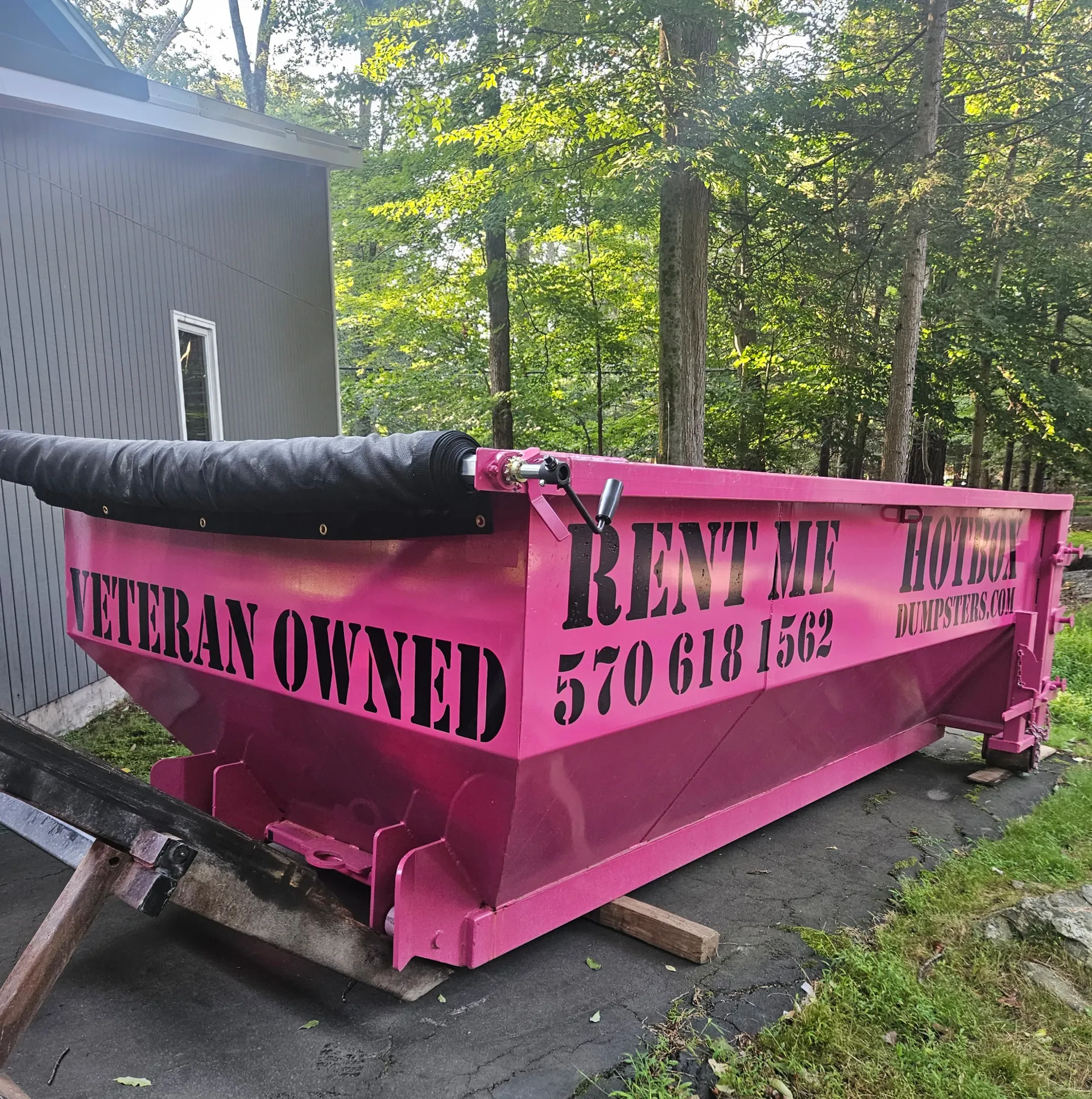 A dumpster is being towed by a dump truck in a driveway.