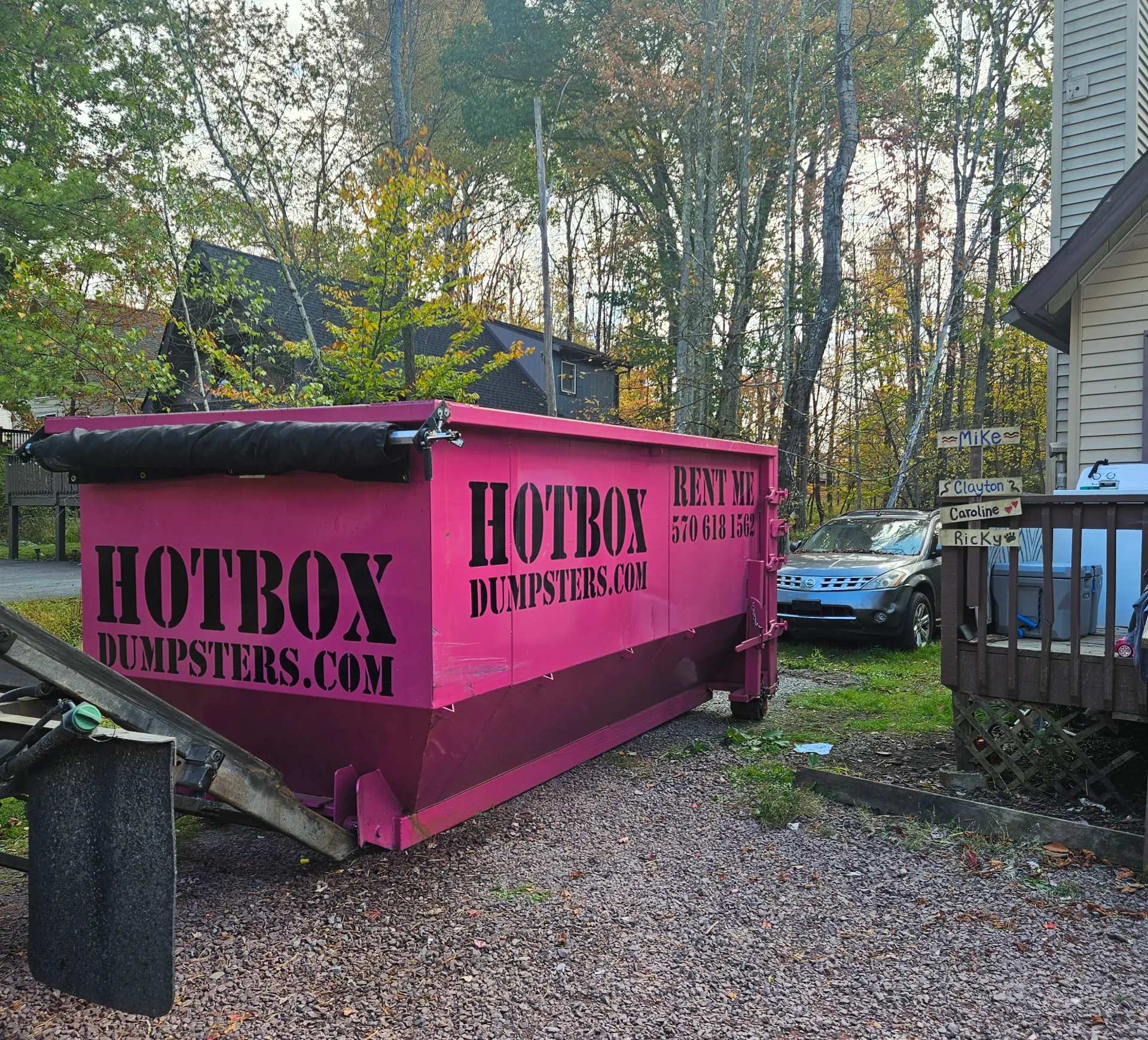A dumpster is being towed by a dump truck in a driveway.