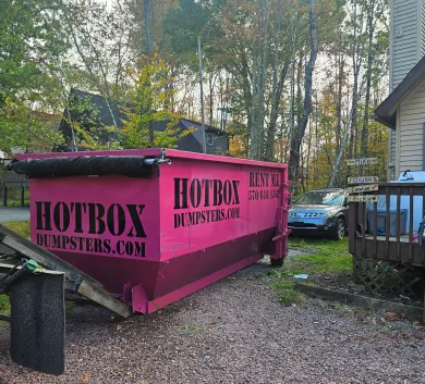A green dumpster is parked in front of a rose nail salon.