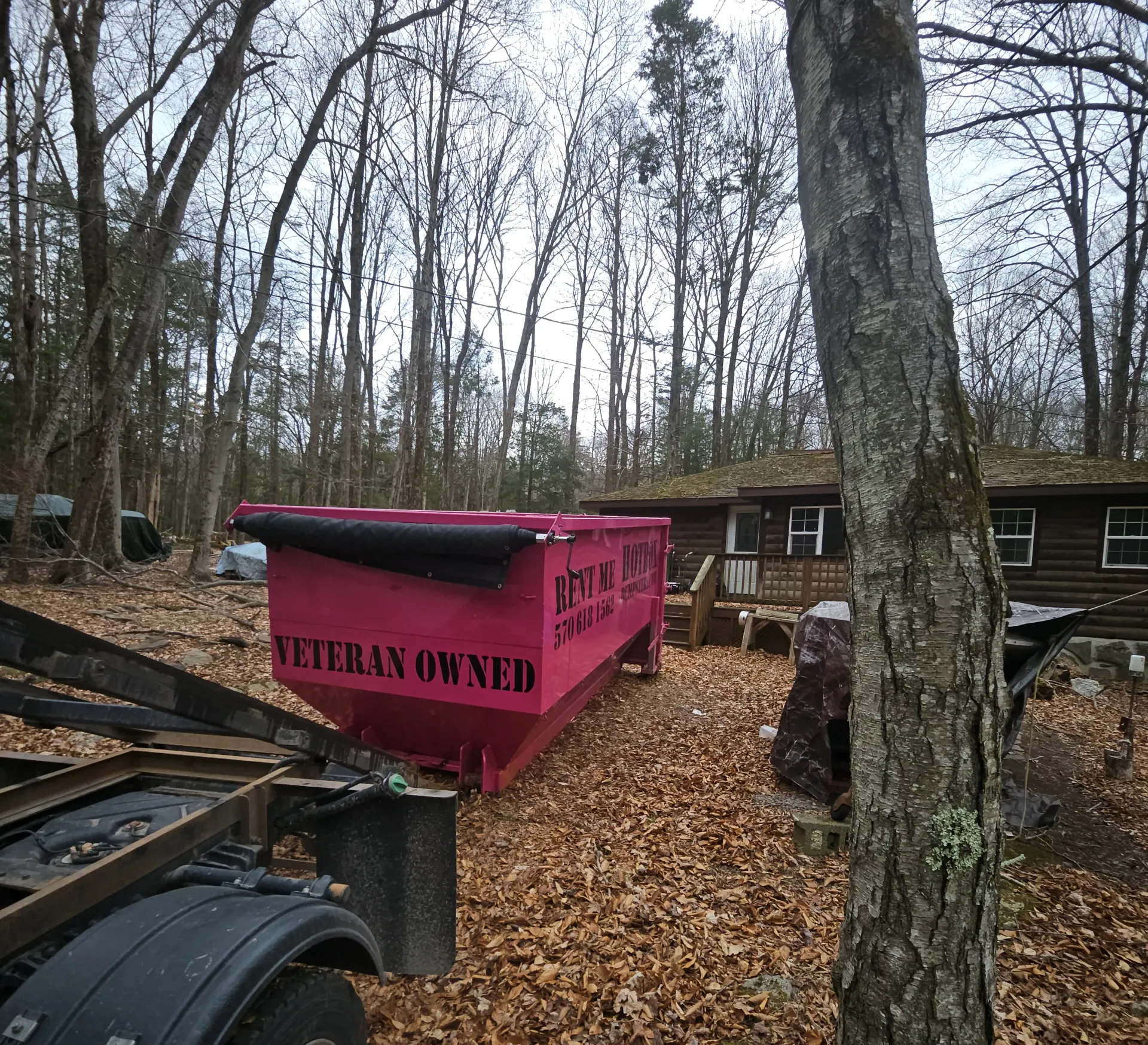 A green dumpster is sitting on the side of a truck in front of a house.