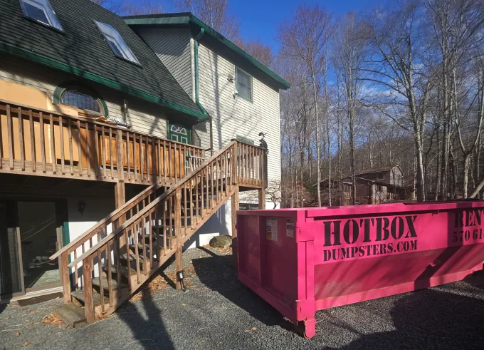 A green dumpster is parked in front of a house.