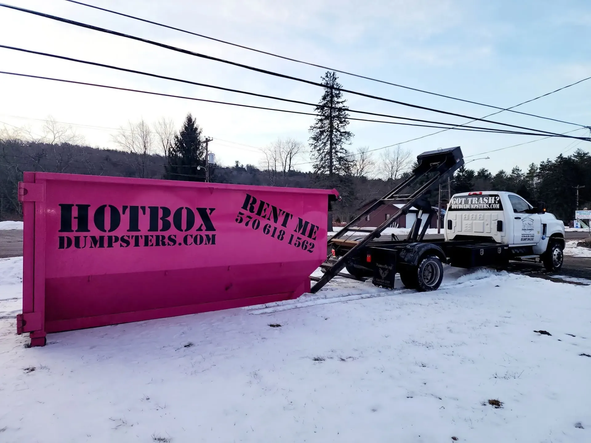 A dumpster is being towed by a dump truck in a driveway.