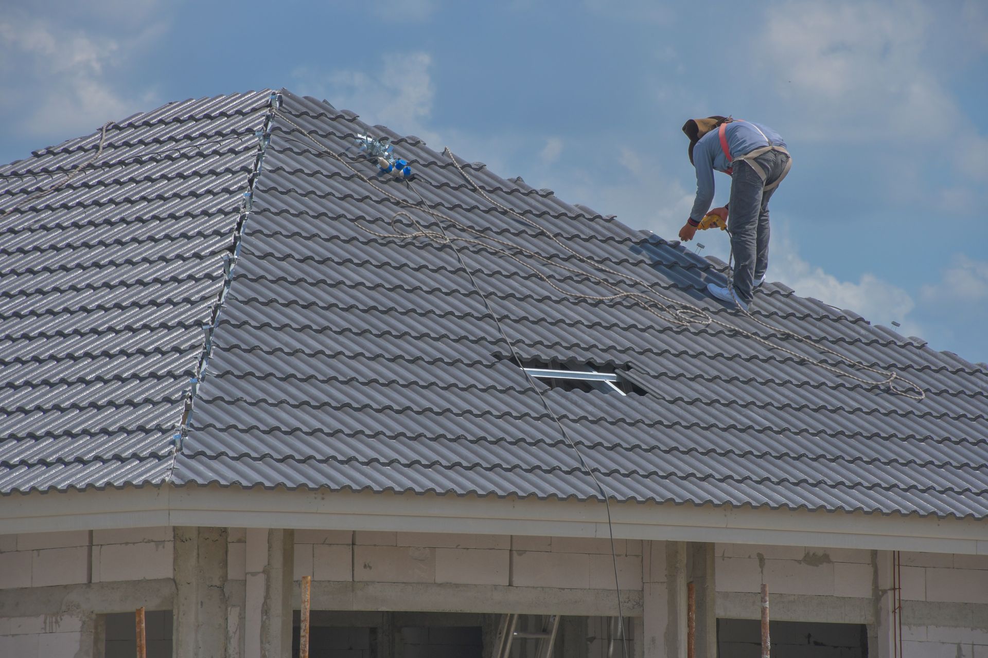A construction worker is installing tile on the roof of a large house.